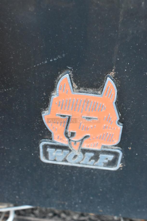 Wolf Metal logo on a commercial gas-powered 6 burner range with flat top griddle, oven, backsplash, and overshelf.