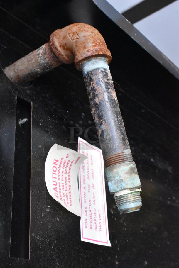 Wolf metal gas range with 6 burners, flat top griddle, oven, back splash, over shelf. Rust on pipe fitting. Caution label.