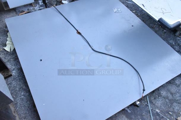 Gray metal panel featuring a hole, visible cable, and minor surface marks. Condition suggests use; ideal for industrial applications.