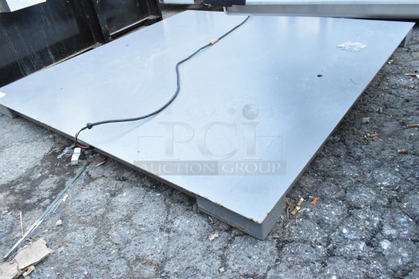 Gray metal panel, rectangular shape, with visible wiring on concrete ground. Some wear and surface markings.