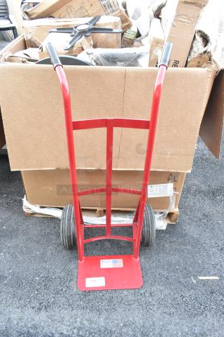Milwaukee red metal hand truck, sturdy design, rubber handles, large wheels, labeled with Milwaukee logo and U.S. flag.