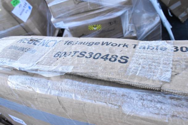 Cardboard box labeled "Regency 16 Gauge Work Table 600TS3048S," indicating a scratch and dent item. Box appears sealed.