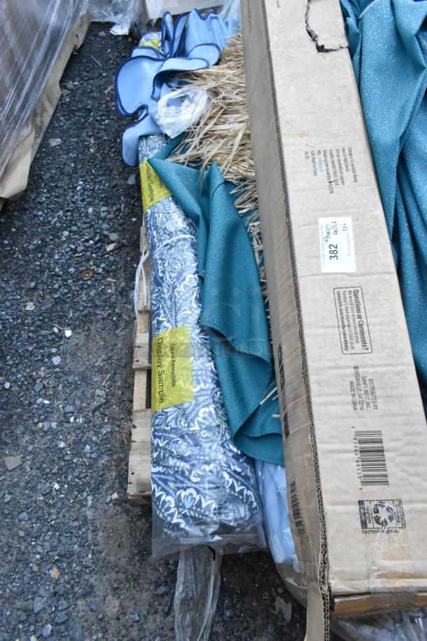 Pallet lot with assorted items including a blue floral patio umbrella, fabric swatches, and boxed items. Tags: "Display Sample."