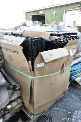 Pallet of black metal wire racks, brand new with scratch and dent, in large cardboard box, some stacking visible.