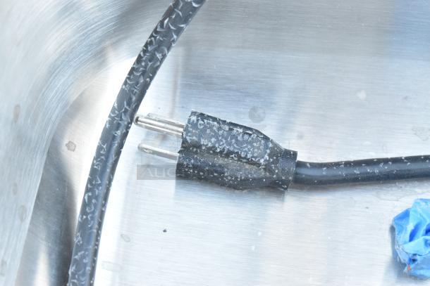 Stainless steel portable sink surface with a power cord and visible wear, highlighting its commercial functionality.