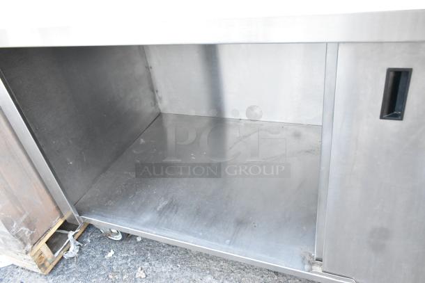 Win-holt stainless steel counter with 2 doors, under shelf, and commercial casters. Visible wear; suitable for storage.