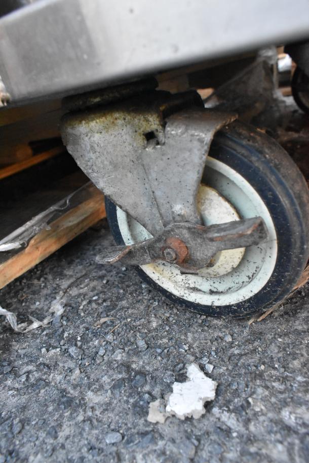 Win-holt stainless steel counter wheel with brake, shows signs of wear, mounted on commercial casters for mobility.