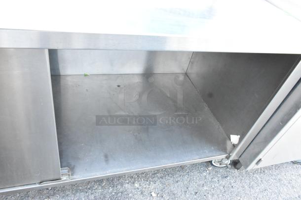 Win-holt stainless steel counter with two doors, under shelf, commercial casters, and visible wear on interior.