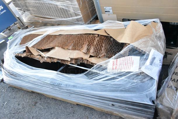 Black metal locker in packaging, secured with plastic wrap and cardboard. Visible handling instructions on label. New condition.