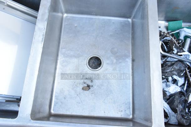 Winholt stainless steel 3-bay sink with dual drain boards, no legs, evident wear and some debris in sink.
