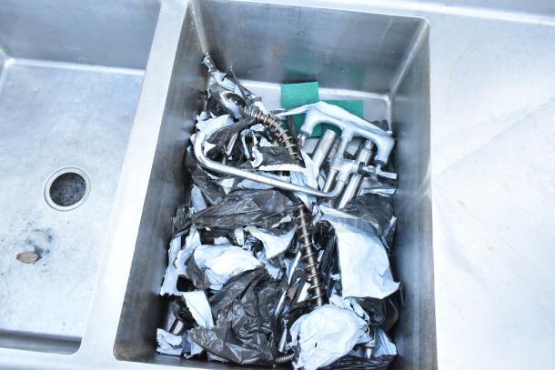 Winholt stainless steel 3-bay sink with dual drain boards, missing legs, includes wrapped faucets and hardware in basin.