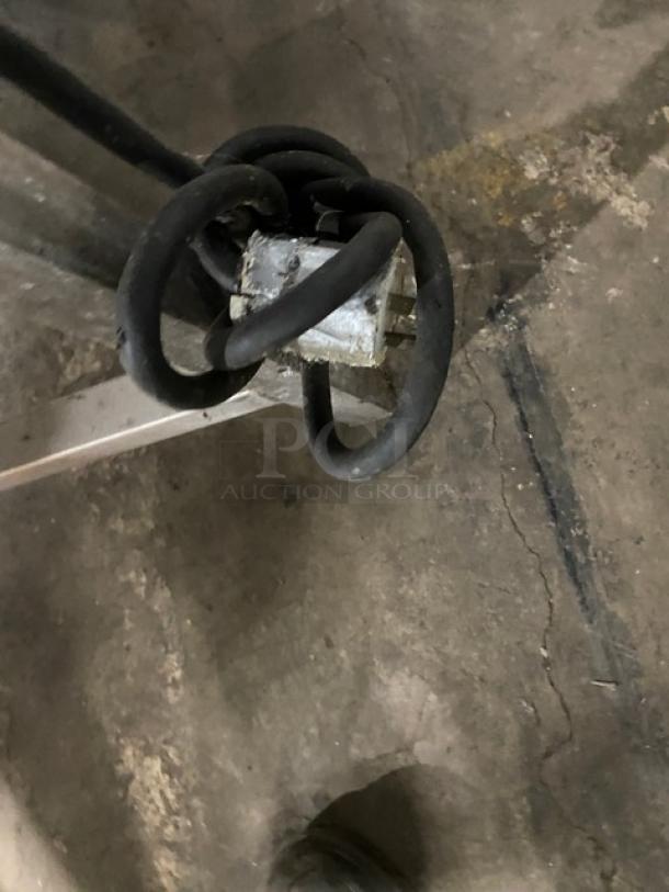 Coiled black electrical cord with a metal connector on the end, resting on a concrete floor.