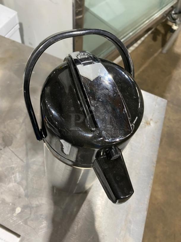 Stainless steel insulated beverage dispenser with black lid and handle, features spout for easy pouring. Good condition.