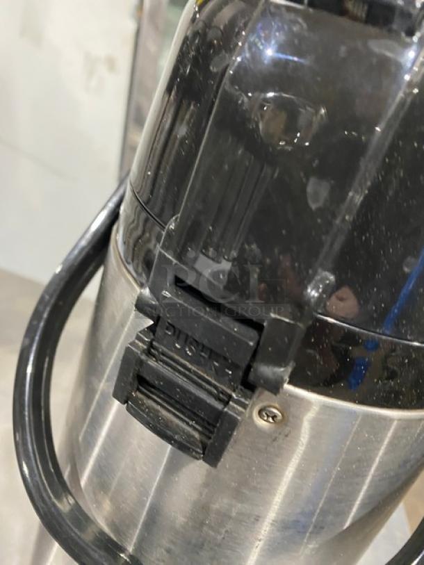 Commercial stainless steel insulated beverage dispenser, black plastic lid, and handle. Features a push-button spout. Slightly worn.