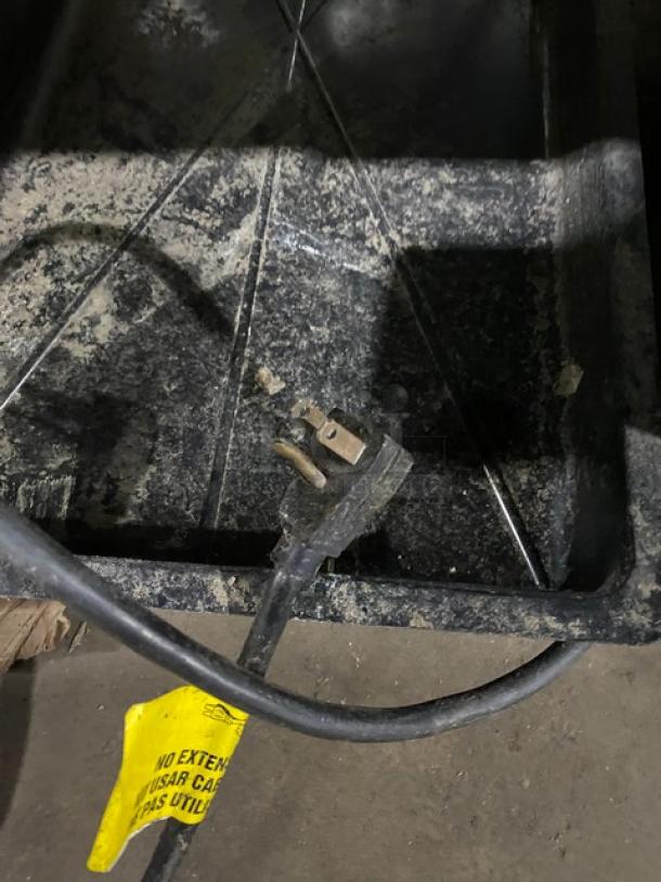 Alt text: Black power plug on a gray surface with a yellow caution label attached.