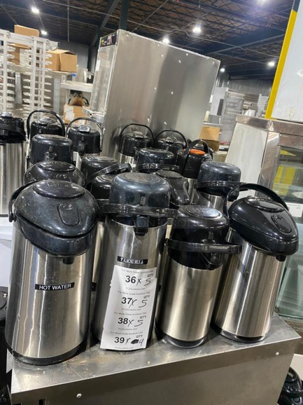 Stainless steel insulated beverage dispensers on a metal counter. Multiple units labeled for hot liquids. Auction item.