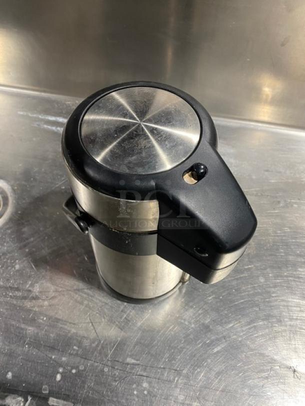 Stainless steel insulated beverage dispenser with black handle in good condition on metallic surface.