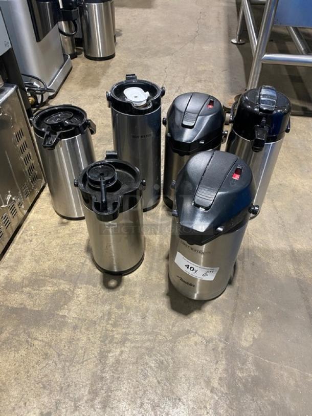 Stainless steel insulated beverage dispensers, commercial grade, six units, varying lids, tags indicate bid information.