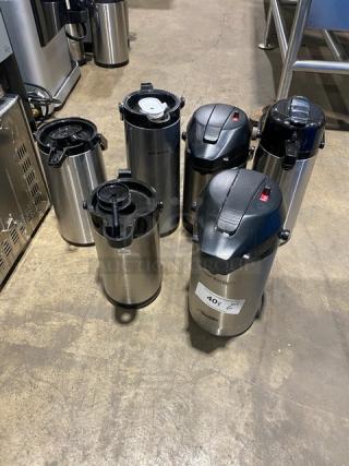 Stainless steel insulated beverage dispensers, commercial grade, six units, varying lids, tags indicate bid information.