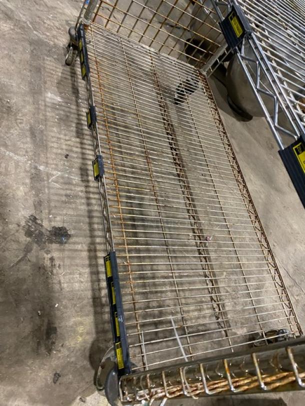 Commercial 4-tier mobile storage cart with enclosed wired-rack design, on casters. Metal construction, signs of rust.