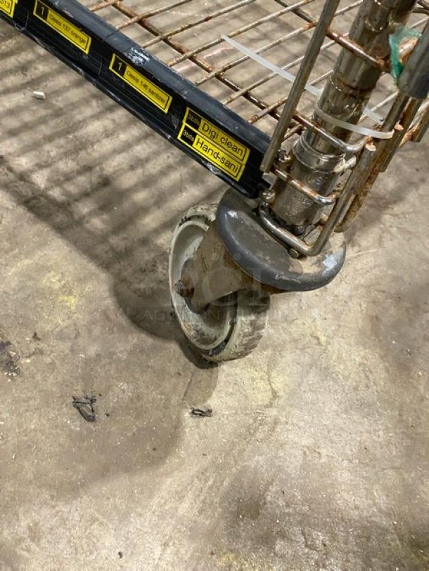 Commercial 4-tier mobile storage cart with enclosed wired racks, on casters. Visible wear and rust on wheel and wiring.