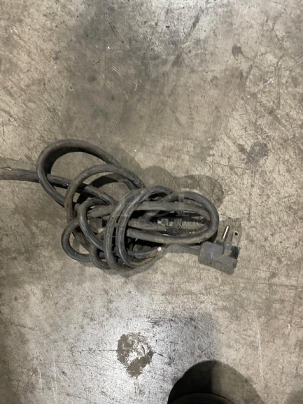 Coiled power cord on the floor, possibly for an appliance or equipment. Plug is visible. Floor appears industrial.