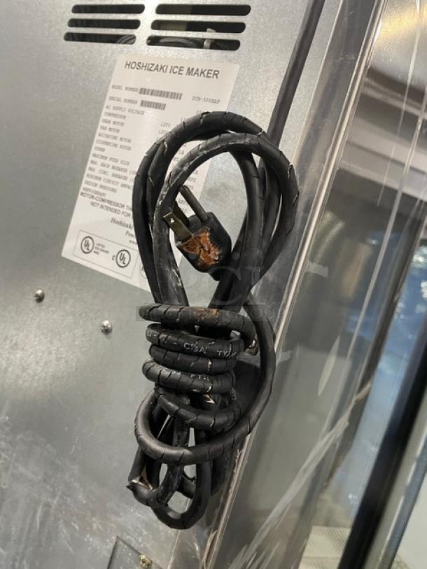 Hoshizaki DCM-500BAF ice maker, stainless steel, air-cooled, electric, with drip tray. Includes power cord, some wear visible. Model and specs printed on label.