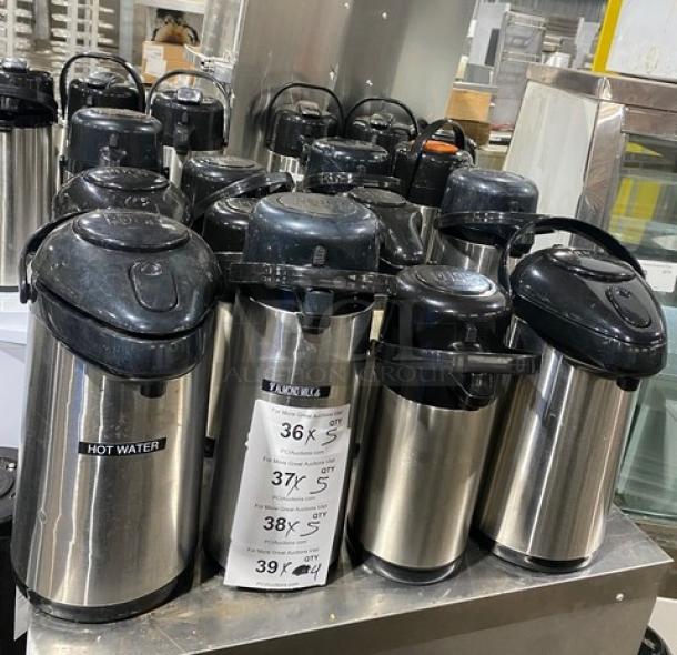 Commercial stainless steel insulated beverage dispensers, multiple units. Black lids, "Hot Water" label on some. Ideal for catering.
