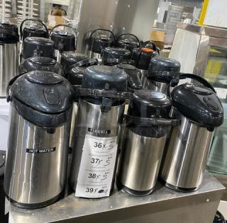 Commercial stainless steel insulated beverage dispensers in good condition, multiple units, black lids, various sizes labeled.