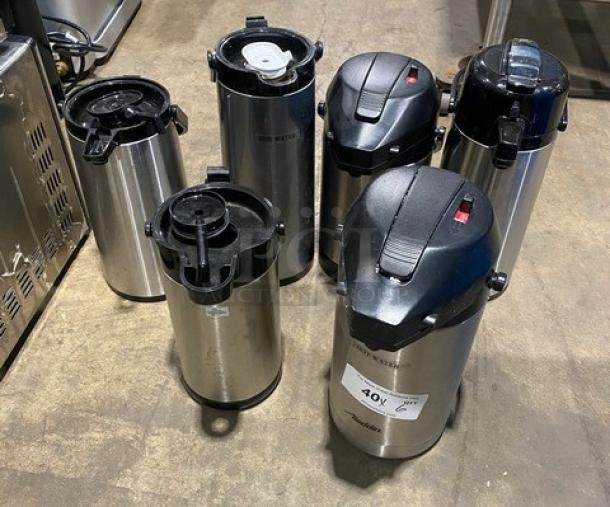 Stainless steel insulated beverage dispensers, commercial grade, six units, varying lids, tags indicate bid information.