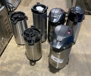 Stainless steel insulated beverage dispensers, commercial grade, six units, varying lids, tags indicate bid information.