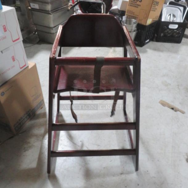Wooden high chair with safety straps, brown finish, sturdy design, gently used condition, suitable for infants.