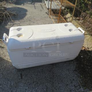 White Igloo cooler with handles, lid cup holders, visible scuffs. Brand name "Igloo" imprinted on lid. Used condition.