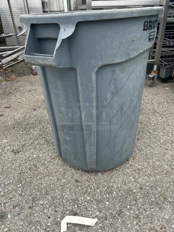 Rubbermaid Brute trash can, gray, with visible scuffs. Durable plastic, side handles. Ideal for industrial use.