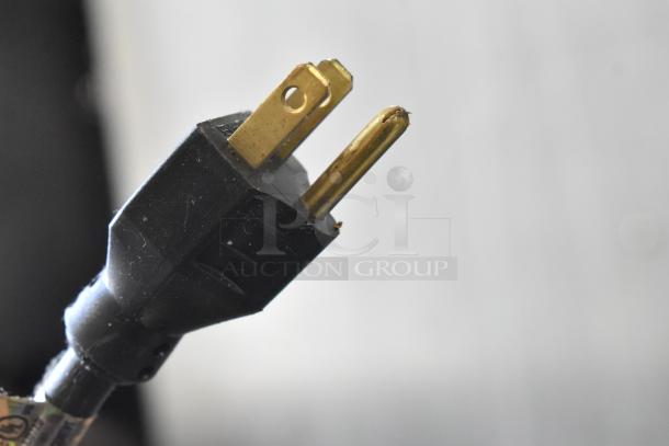 Close-up of a black plug with two gold prongs, showing minor wear. No specific details about the Groen steam kettle here.