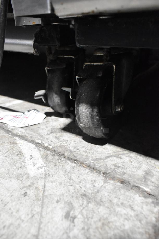 True T-35 commercial cooler caster wheels on a concrete floor, showing wear. Durable mobility for easy transport.