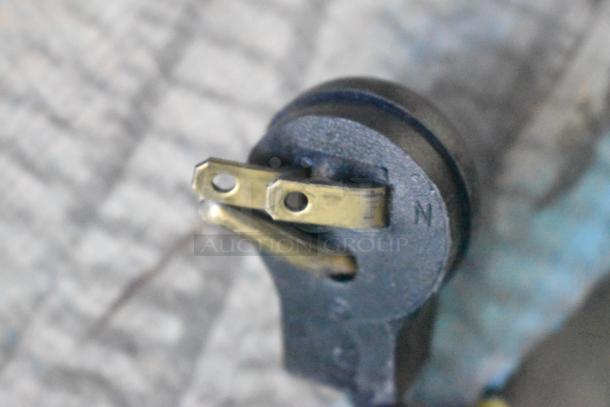 Close-up of a power plug from an Imbera EVC04 mini cooler, showing two prongs and an "N" marking on a metal background.