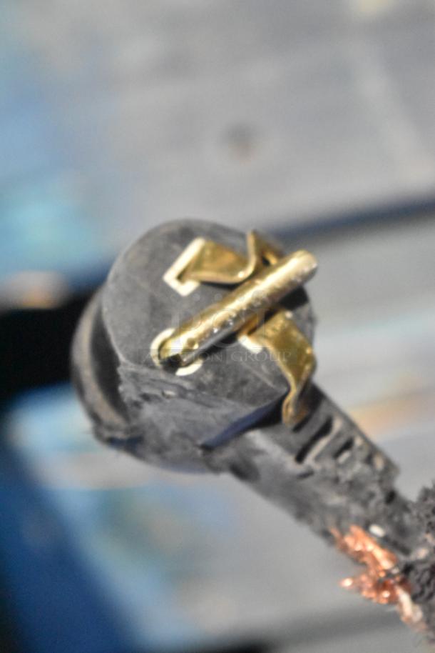A black and gold electrical plug, possibly for a vending machine, with visible wear and copper wiring exposed at the base.