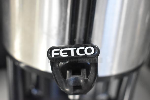 Fetco stainless steel beverage dispenser with branded handle. Excellent condition, ideal for commercial use.