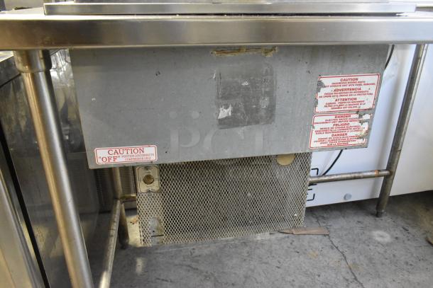 Stainless steel commercial work table with drop-in unit, 115 volts, 1 phase. Visible caution labels and metal mesh panel.
