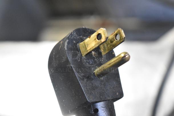 Close-up of a used black power plug, part of a stainless steel commercial work table, 115 volts, 1 phase.