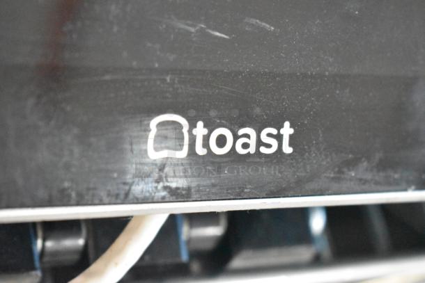 Toast POS monitor close-up showing logo with slight surface wear. Part of auction lot including receipt printers and more.