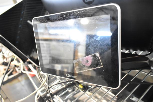 Toast POS monitor with visible screen wear, set on a metal rack. Includes cables. Part of an 8-item auction lot.