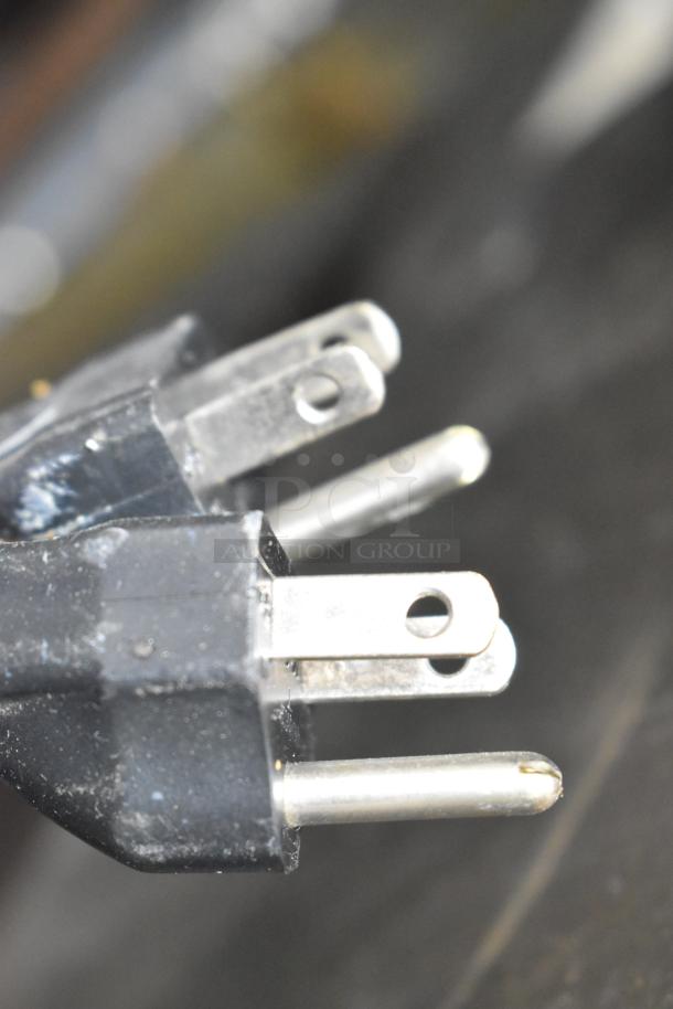 Close-up of a power plug with three prongs, indicative of an electrical connection. Black plastic casing with visible wear.