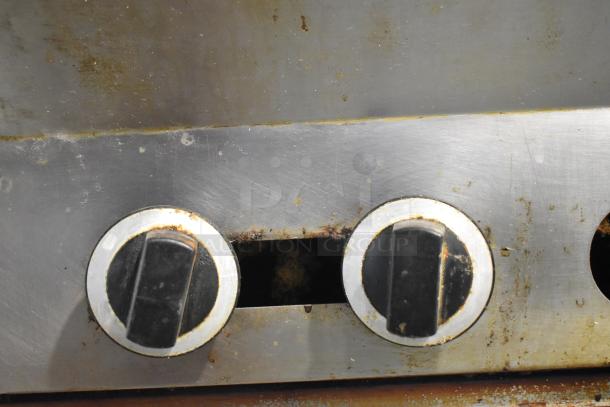 US Range stainless steel commercial gas range detail, two burner knobs shown with signs of wear, indicating use.