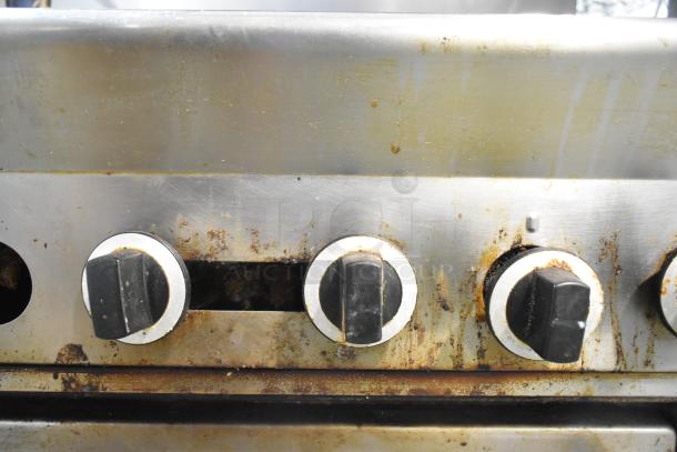 US Range commercial gas range with six burners, oven, overshelf, and backsplash. Stainless steel, visible wear and rust.