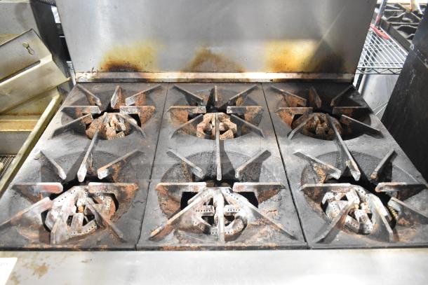 US Range stainless steel commercial gas 6-burner range with oven, overshelf, and backsplash. Shows signs of wear.