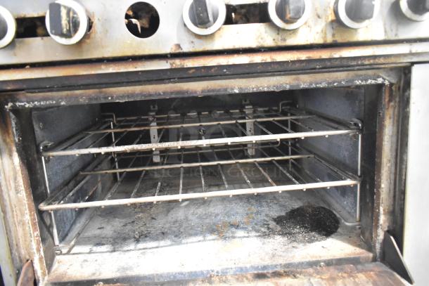 US Range stainless steel commercial gas-powered 6-burner range with oven. Features overshelf and backsplash. Used condition.