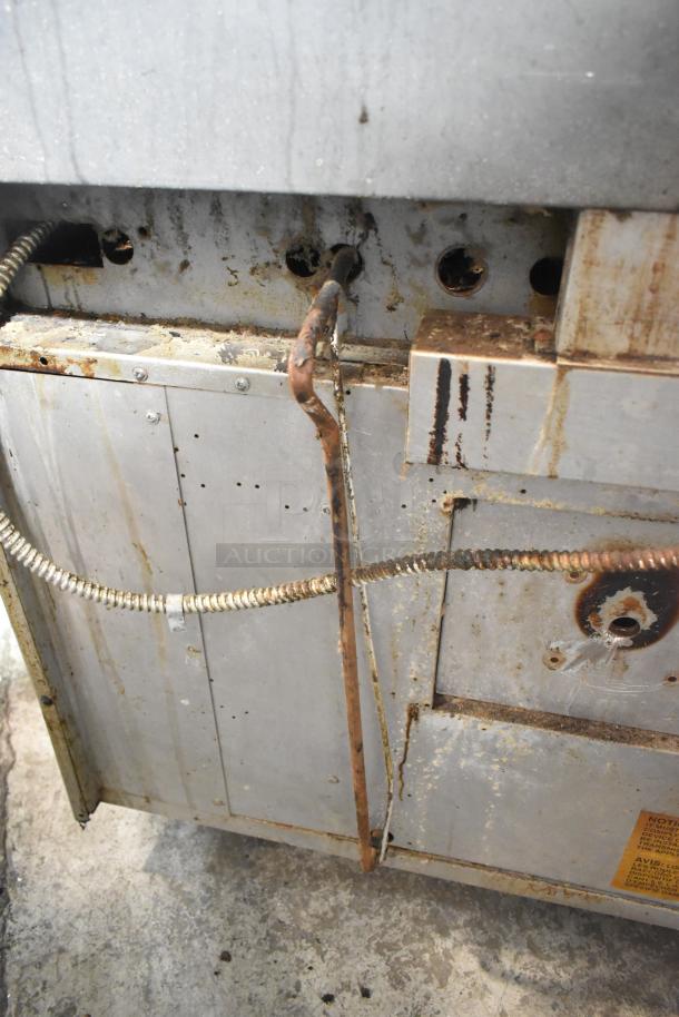 US Range stainless steel commercial gas-powered 6 burner range with oven, over shelf, and back splash, showing wear and rust.