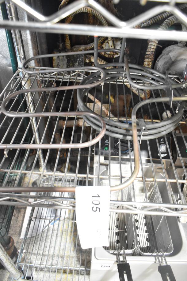 Two metal burners on a wire rack, industrial setting. Label marked "105" attached. Condition appears used.
